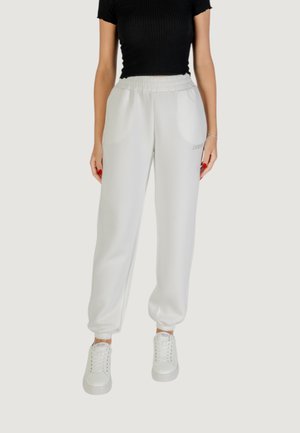 Pantaloni sweatpants bianchi con vita elastica, tasche laterali e polsini, caratterizzati da un sottile dettaglio del logo. Abbinati a sneakers bianche e una maglietta nera.