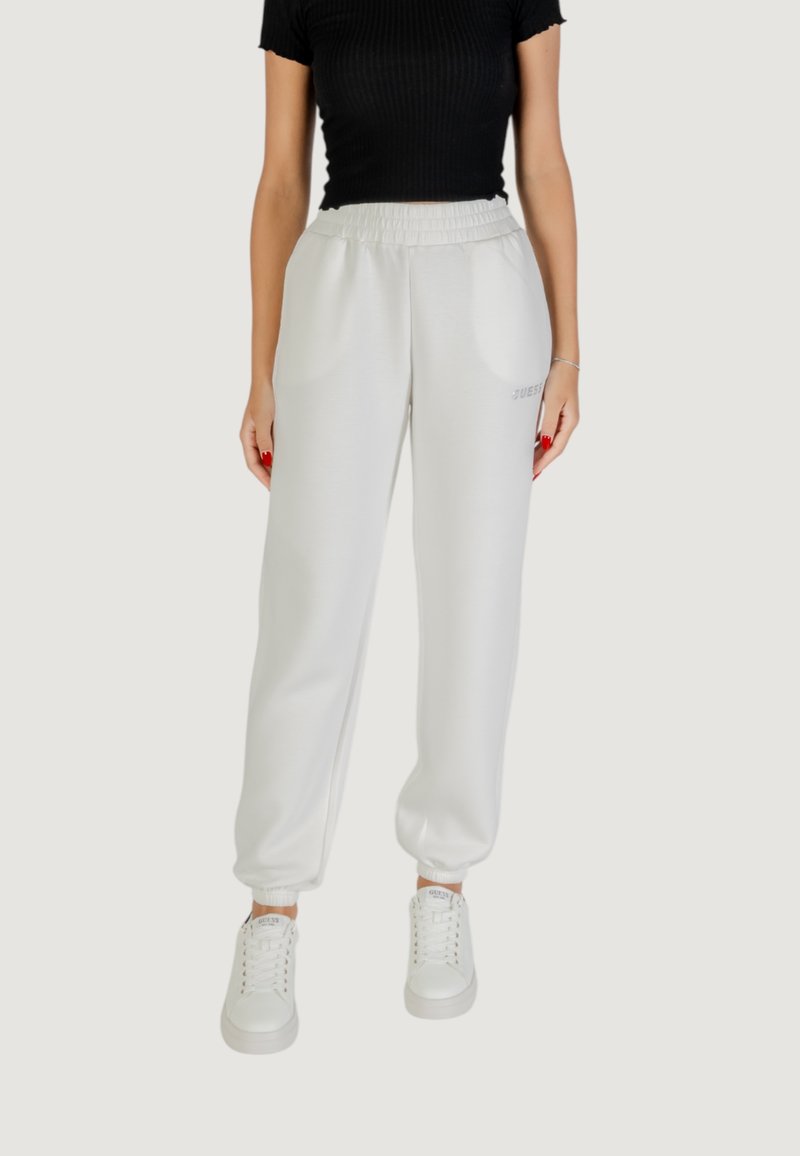 Pantalons de survêtement blancs à taille élastique avec poches latérales et poignets, arborant un discret logo. Associés à des baskets blanches et un haut noir.