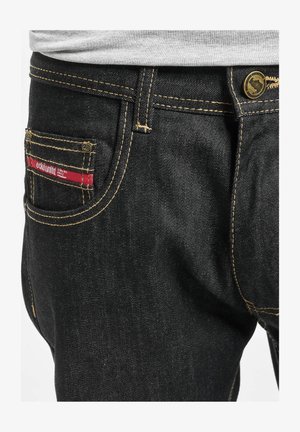 Mustad denim püksid kontrastsete kollaste õmblustega, punase sildiga tagaosal, ning metallist nööpkinnitusega vöökohal.