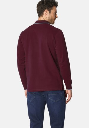Langärmliges Poloshirt aus dunkelburgunderfarbigem Baumwollstoff, mit einem klassischen Kragen in Blauakzenten und geradem Saum, kombiniert mit blauen Jeans.