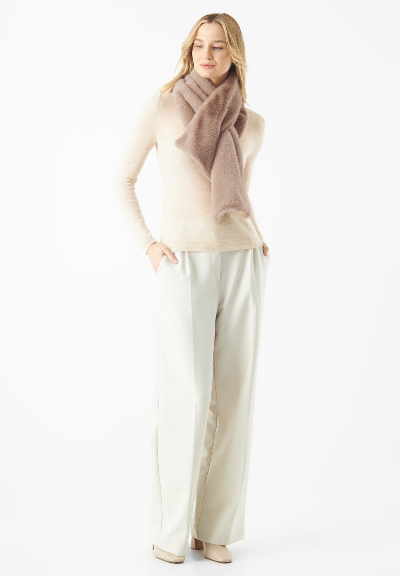 Pull beige à manches longues, associé à un pantalon large de couleur pâle. Une écharpe douce et marron clair s'enroule élégamment autour du cou.