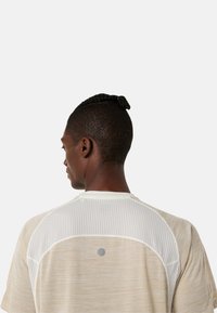 T-shirt de sport clair avec un tissu texturé, des détails en maille sur les épaules et un logo circulaire au dos.