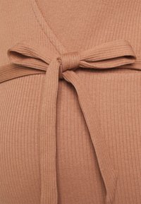 Tecido canelado numa tonalidade terracota quente, com um detalhe de cinto atado à cintura. A textura parece suave e elástica.
