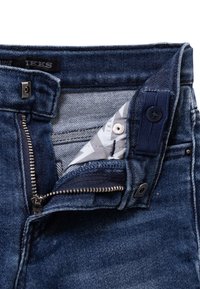 Donkerblauwe spijkerbroek met een ritssluiting en knoopsluiting. De tailleband heeft een gemusterde binnenvoering. Een zichtbaar ritsdetail is te zien.