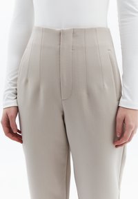 Beige op maat gemaakte broeken met een hoge taille, voorzien van verticale naden en zijzakken. Glad textuur en gestructureerd silhouet.