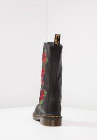 Botte en cuir noir montée jusqu'au genou, ornée de broderies de roses rouges, avec des coutures jaunes le long de la semelle et une languette au sommet.
