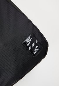 Bolsa de tela negra texturizada con un parche rectangular del logo de Nike Air Max que presenta letras blancas y un diseño de rayas como acento.