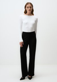 Haut à manches longues ribé blanc associé à un pantalon large noir taille haute et des escarpins noirs à bouts pointus, design minimaliste, sans motifs.