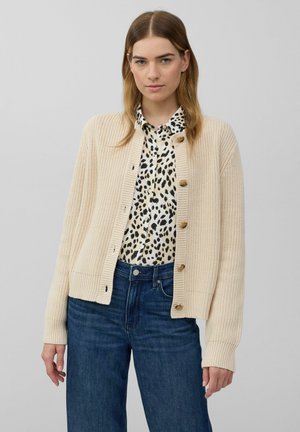 Beige gestrickte Cardigan mit gerippter Textur, Knopfverschluss und langen Ärmeln, getragen über einem Schwarz- und Creme-farbenen Leopardenmusterhemd.