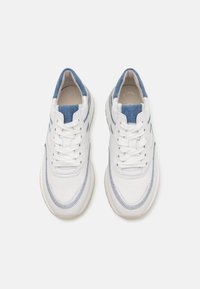 Baskets blanches avec des accents en denim, présentant un bout rond, un matériau texturé, un laçage à l'avant et des détails de couture contrastants.