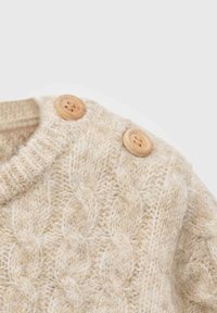 Kremno obarvan pleteni pulover z rameni in dvema velikima lesenima gumboma ter kabelskim pletenjem iz mehkega volnenega materiala.