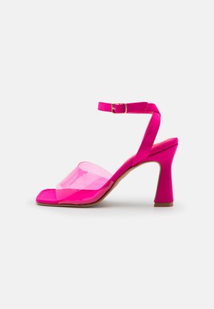 Pink heeled sandal with a clear plastic strap, open toe design, and a slender block heel, featuring a buckle ankle strap.