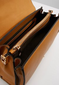 Borsa a mano in pelle marrone con una texture liscia, profili neri, tasca con zip e dettagli in metallo dorato, dotata di più scomparti interni.