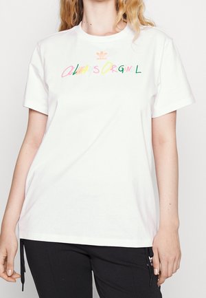 Biała bawełniana koszulka z wielokolorowym napisem "Zawsze Oryginalny" w zabawnym kroju czcionki oraz logo adidas powyżej w kolorze pomarańczowym.