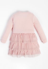 Růžové šaty s obepnutým topem a dlouhými rukávy. Sukně má několik vrstev volánků vyrobených z třpytivé tylové látky.