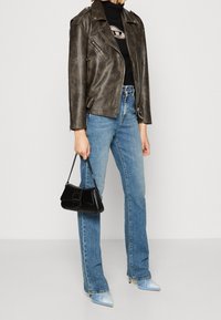 Veste de moto en cuir marron, col roulé noir, jeans évasés bleu clair, sac à main noir et escarpins avec des accents bleus.