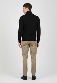 Czarny sweter z długim rękawem i wysokim kołnierzem, z prążkowanym dołem i gładką teksturą, zestawiony z beżowymi, dopasowanymi spodniami i czarnymi butami.