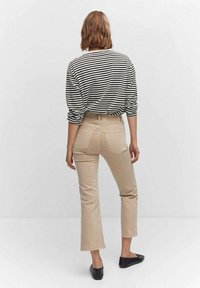 Camisa de rayas en blanco y negro de manga larga combinada con pantalones acampanados beige. La tela parece suave; los pantalones tienen un dobladillo sin acabar y bolsillos clásicos.