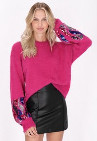 Fuzzy roze trui met lange mouwen, versierd met kleurrijke paillettenspatters; gecombineerd met een zwart leren minirok.