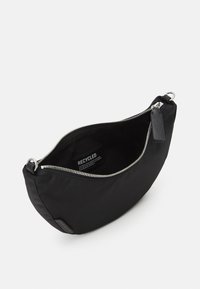 Musta kierrätetystä kankaasta valmistettu laukku, jolla on pyöreä muoto, hopeinen vetoketju ja nahkainen merkki. Sisäpuolen etiketti näkyvissä. Suora pinta, minimalistinen muotoilu.