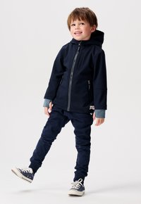Hoodie navy avec fermeture éclair et poches latérales, associé à un jogger navy assorti. Le design des poignets gris et des baskets blanches complètent le look.