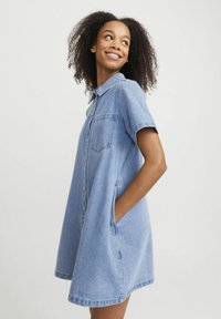 Kambro suknelė, trumpomis rankovėmis, suknelė su mygtukais priekyje, apykaklė, laisvas siluetas, iki kelių ilgio, šoninės kišenės, šviesiai mėlyna spalva, džinsinio audinio tekstūra.