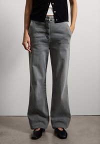 Grijze wijde jeans van denim, met een hoge taille, zijzakken en subtiele vervaging langs de benen. Gepaard met zwarte schoenen.