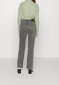 Light green ribbed sweater paired with high-waisted, straight-leg gray jeans. Notable back pocket stitching and chunky heeled shoes.