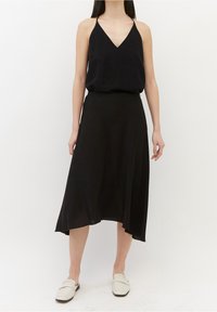 Sort ærmeløs top med V-hals parret med en svævende sort midi-skirt, der har en blød tekstur og en asymmetrisk kant.