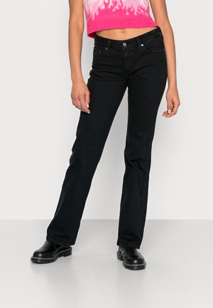 Jeans flare em denim preto com design de cinco bolsos, ajuste de cintura média e costura subtil. Combinados com um suéter cropped rosa com vários padrões.