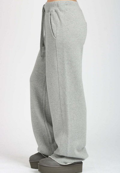 Pantaloni della tuta grigi chiari con vestibilità rilassata, vita con cordoncino, tasche laterali e morbida texture del tessuto. Abbinati a scarpe con zeppa grigia.