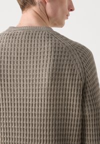 Strickpullover in einem hellbraunen Farbton mit einem strukturierten, gerippten Muster. Verfügt über einen Rundhalsausschnitt und Raglanärmel.