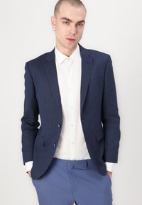 Navy blue, textured blazer with two buttons, paired with a white button-up shirt. Light blue trousers complete the outfit.