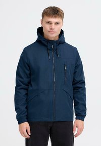 Mornarsko modra zip-up jakna s kapuco, ki ima žep na prsih in elastične manšete. Gladka tekstura z minimalističnim dizajnom in šivnimi detajli.