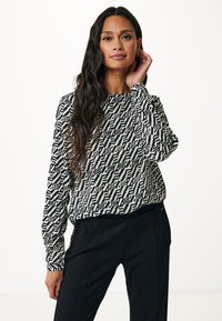 Maglietta a maniche lunghe bianco e nero con un fit morbido, caratterizzata da design geometrici e un collo rotondo, abbinata a pantaloni neri.