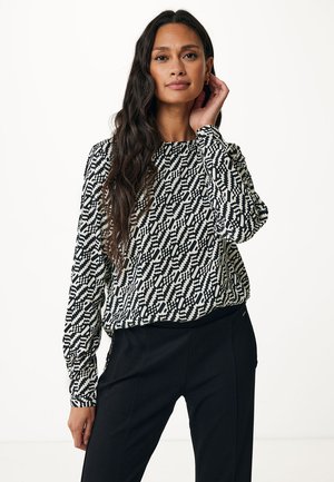 Maglietta a maniche lunghe bianco e nero con un fit morbido, caratterizzata da design geometrici e un collo rotondo, abbinata a pantaloni neri.