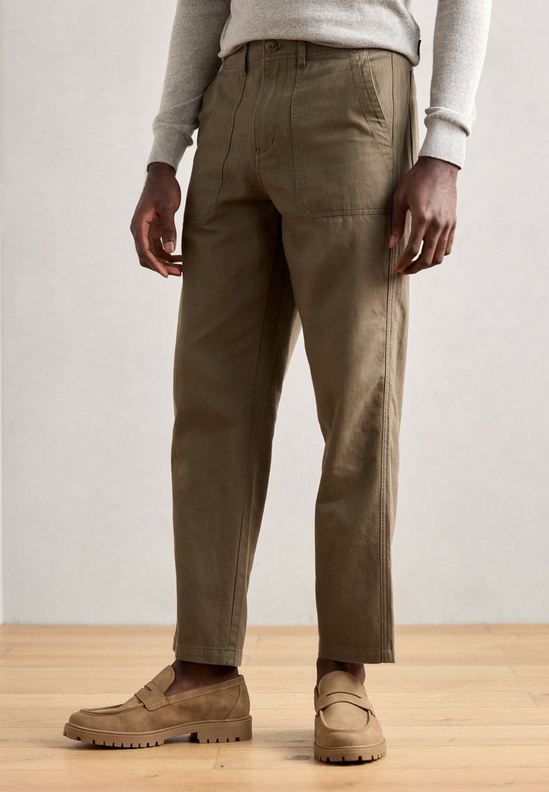 Khaki bukser med en afslappet pasform, der har flade forlommer, subtile syninger og et tekstureret stof. Sæt sammen med beige slip-on sko.