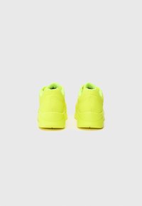 Baskets de sport jaunes vives avec une tige lisse et texturée, un col rembourré et une semelle en caoutchouc. Présente un logo discret à l'arrière.
