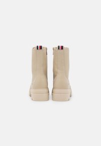 Béžové kotníkové boty z texturované kůže, se zadním zipem, kontrastním červeným a modrým poutkem a silnou krémově zbarvenou podrážkou.