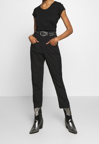 Una camiseta negra de manga corta combinada con pantalones negros de cintura alta. Un cinturón negro con tachuelas ciñe la cintura. Botines plateados de textura completan el look.