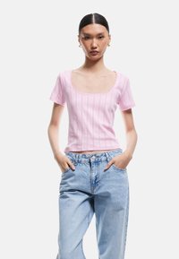 Top corto fitted rosa chiaro con scollo a rotondo, caratterizzato da un motivo testurizzato e bordo in pizzo, abbinato a jeans in denim blu a vita alta.