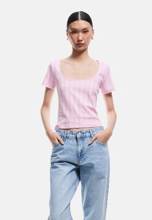 Top corto fitted rosa chiaro con scollo a rotondo, caratterizzato da un motivo testurizzato e bordo in pizzo, abbinato a jeans in denim blu a vita alta.