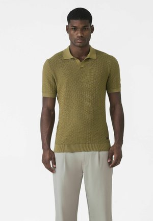 Tricou polo verde texturat cu mâneci scurte, guler și tiv striat. Asocierea cu pantaloni bej îmbunătățește aspectul casual general.