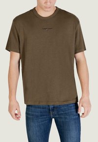 T-shirt verde oliva con scollo rotondo e maniche corte, con un piccolo logo "TOMMY JEANS" in colore a contrasto sul petto.
