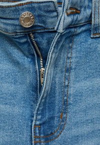 Jeans de denim de culoare albastru deschis au un fermoar metalic cu un mânere argintiu, o închidere mare cu nasture și o cusătură contrastantă de culoare portocalie pe margini.
