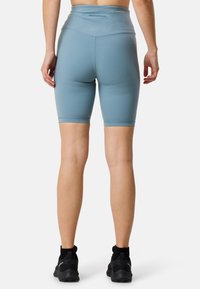 Ljusblå högmidjade cykelshorts med flata sömmar och logotyp på baksidan, kombinerat med svarta träningsskor. Slät, elastisk tyg.