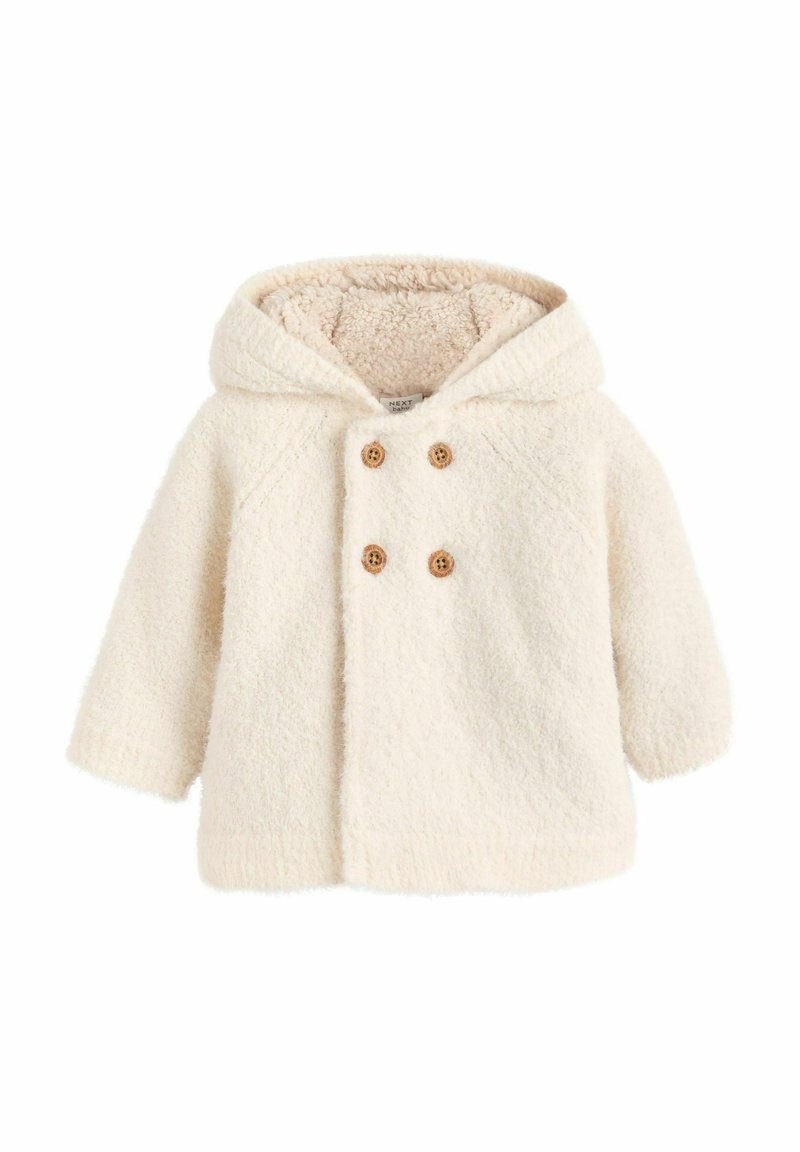 Valge villane kapuutsiga jope, millel on tekstureeritud välimus, kaks puust nuppu ja pehme, karvane vooder. Jope omab raglanvarrukaid ja sirget lõiget.