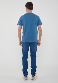 T-shirt in cotone blu con collo tondo classico, abbinato a jeans in denim blu scuro. I jeans presentano una vestibilità affusolata e dettagli di cucitura visibili.