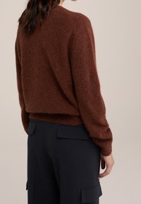 Pull en laine brun, moelleux, avec une coupe décontractée, un col rond et des manches longues, associé à un pantalon cargo noir marine avec poches latérales.