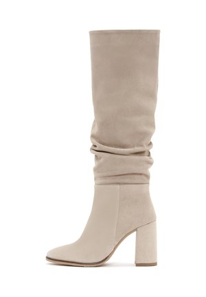 Bottes en suede beige, montant jusqu'au genou, avec un design décontracté, un bout pointu et un chunky talon haut. Texture lisse et accents sans couture.